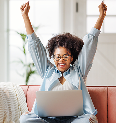 woman sitting on a couch with a laptop on her lap stretching her arms to the ceiling